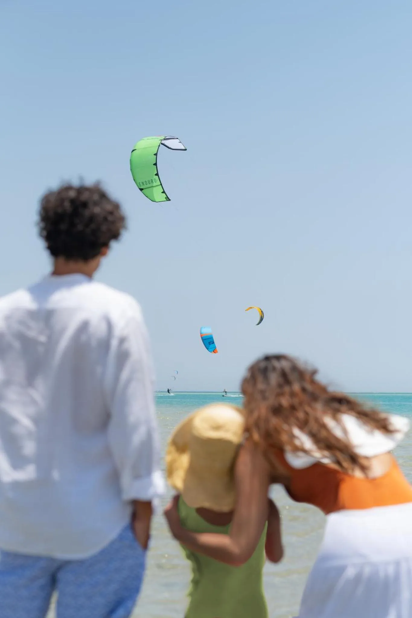 Vue sur la mer avec des personnes au premier plan et des cerfs-volants dans le ciel.
