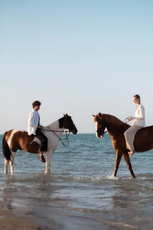 Deux personnes montent à cheval sur une plage.