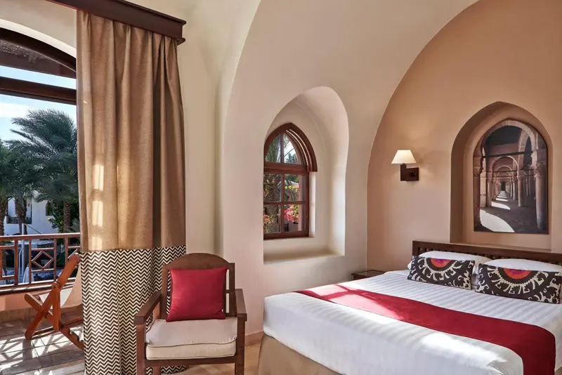 Chambre lumineuse avec un lit confortable et un fauteuil près d'une fenêtre.