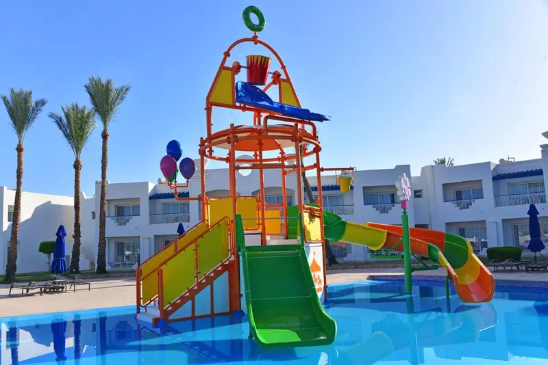 Structure de jeux aquatiques colorée près d'une piscine et de bâtiments.