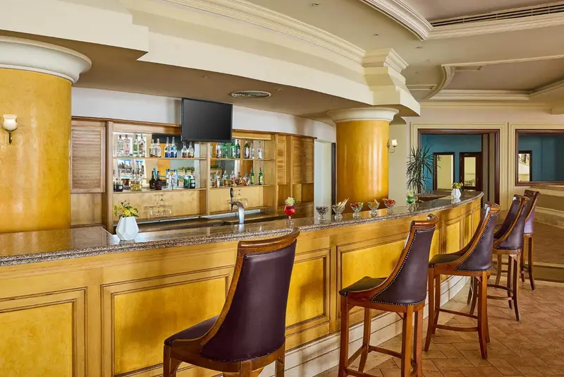 Un comptoir de bar avec des tabourets et des bouteilles est présenté dans un intérieur lumineux.