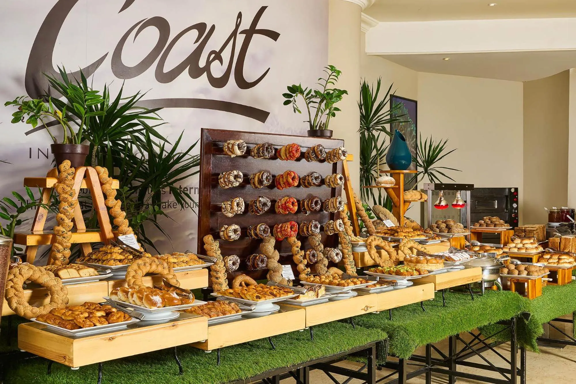 Un buffet garni de viennoiseries et de pâtisseries est présenté sur une table décorée de plantes.