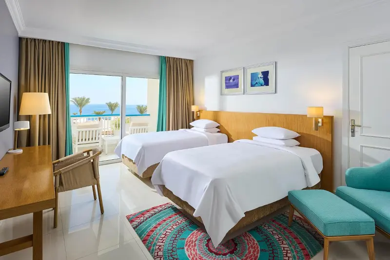 Chambre lumineuse avec deux lits simples et vue sur la mer.