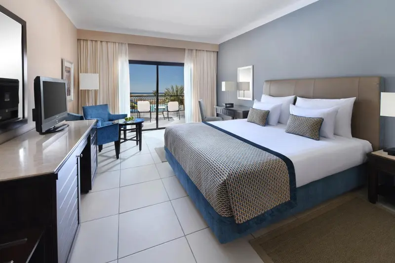 Chambre lumineuse avec un grand lit et un accès à une terrasse.