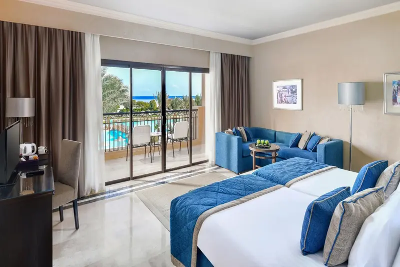 Chambre lumineuse avec un canapé bleu et un accès à une terrasse avec vue sur la mer et une piscine.