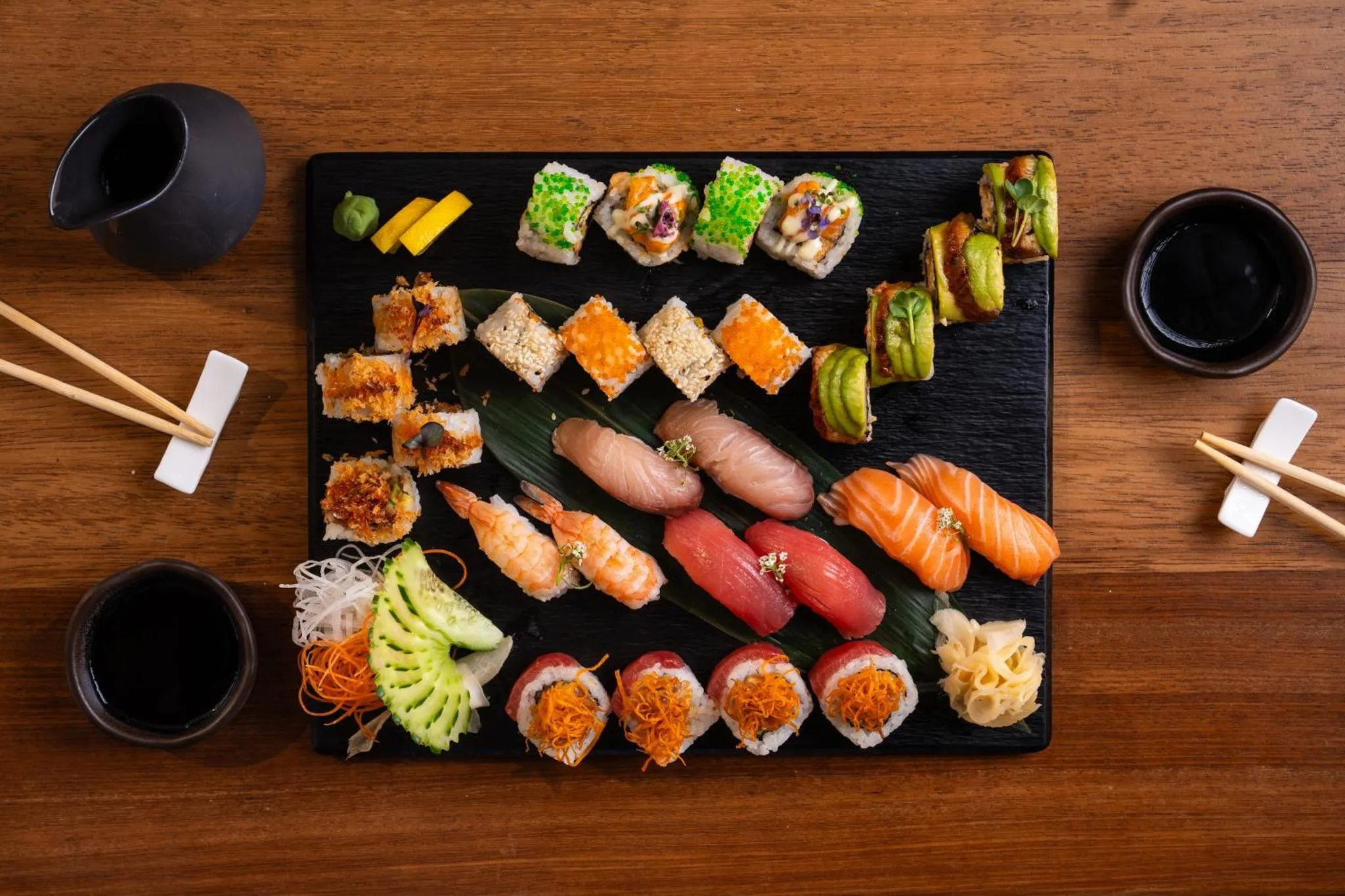 Assortiment de sushis et de makis présentés sur une ardoise noire, accompagnés de sauce soja et de gingembre mariné.