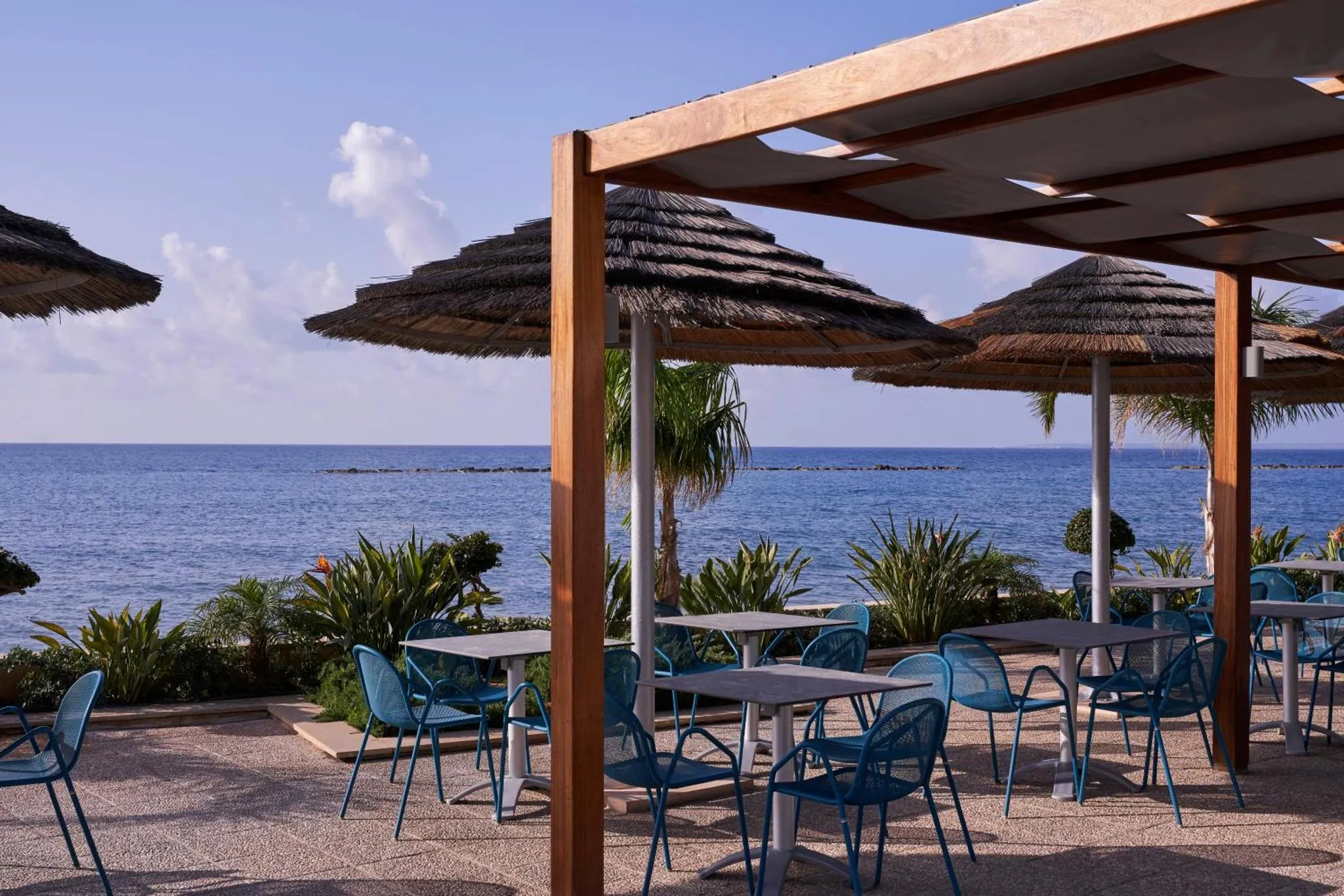 Terrasse ombragée avec tables et chaises face à la mer.