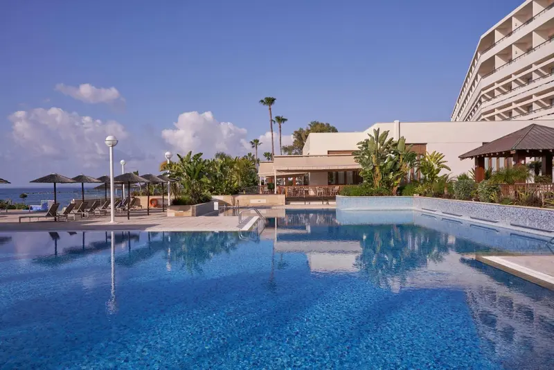 Une piscine bleue reflète un bâtiment blanc et un ciel bleu nuageux.