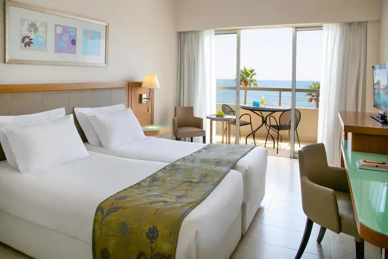 Une chambre lumineuse avec un grand lit et un balcon donnant sur la mer.