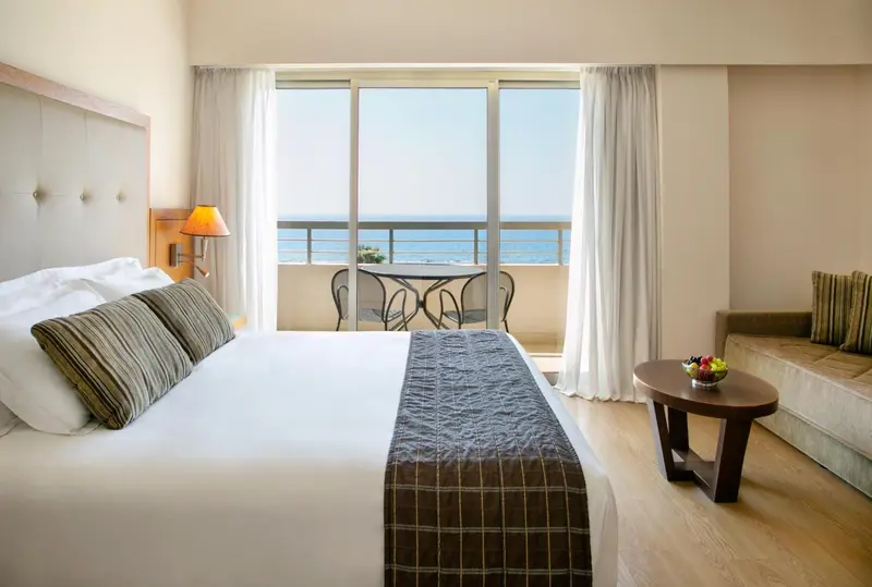 Une chambre lumineuse avec un grand lit donnant sur une vue mer.