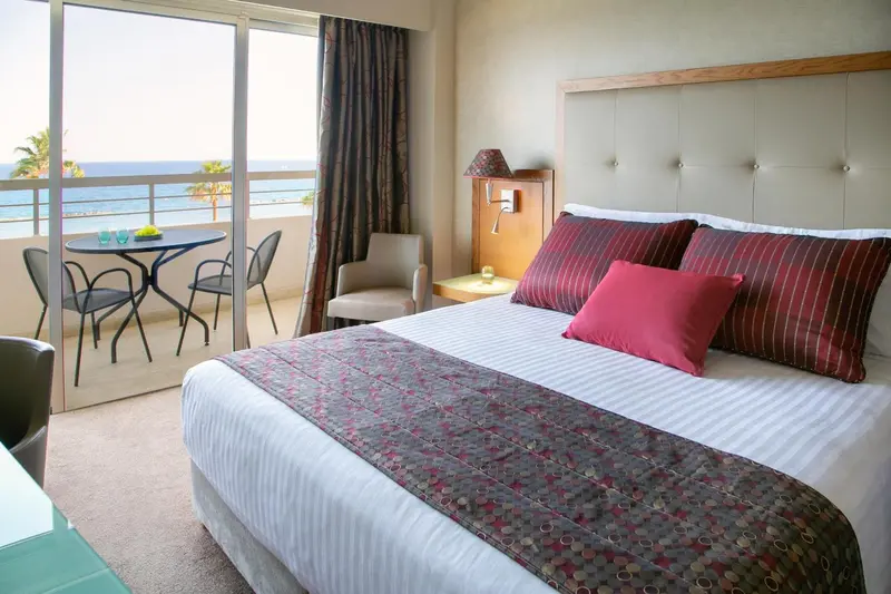 Une chambre lumineuse avec un grand lit et un coin repas donnant sur la mer.