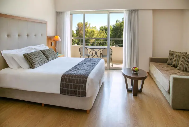 Une chambre lumineuse avec un lit double et un coin salon donnant sur une terrasse.
