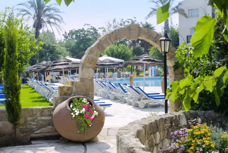 Un arc en pierre donne sur une piscine bordée de transats et de parasols.