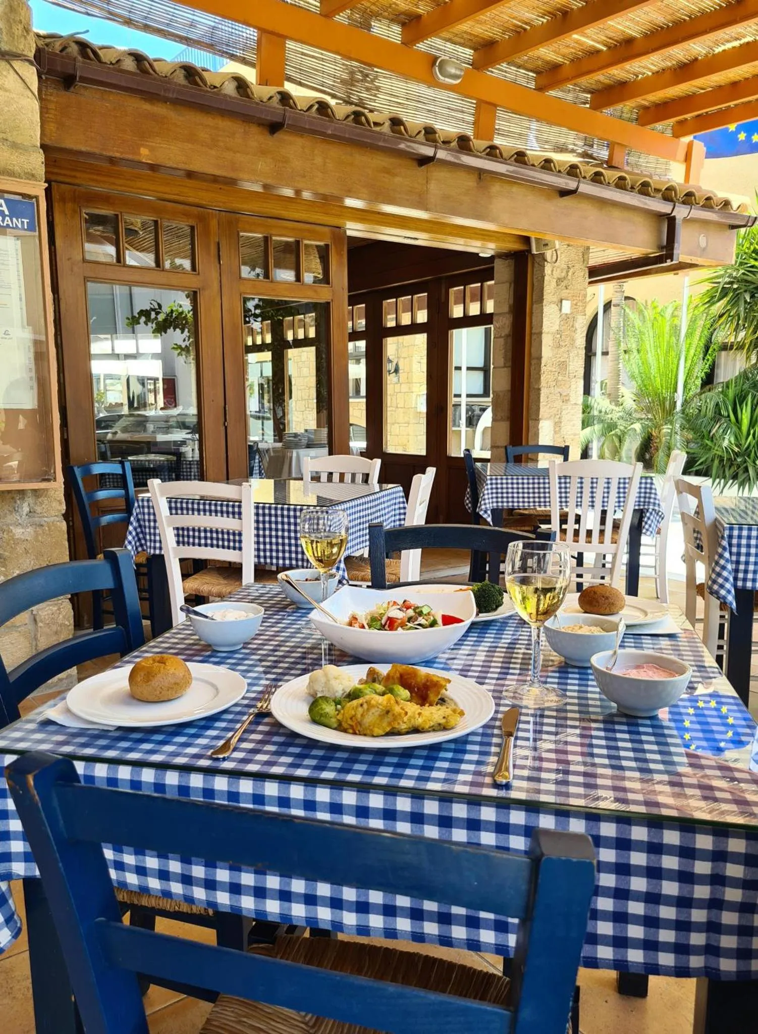 Une table est dressée avec des plats et des boissons sur une terrasse ombragée.
