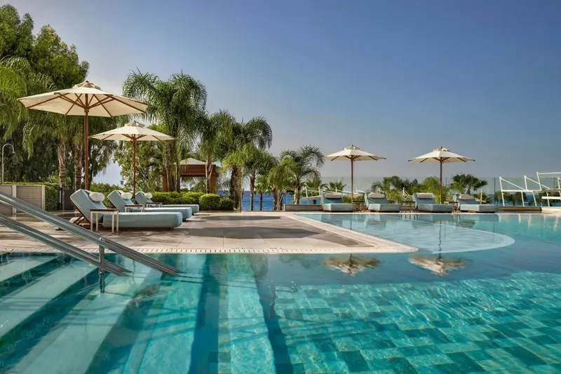 Transats blancs disposés au bord d'une piscine turquoise sous des parasols.
