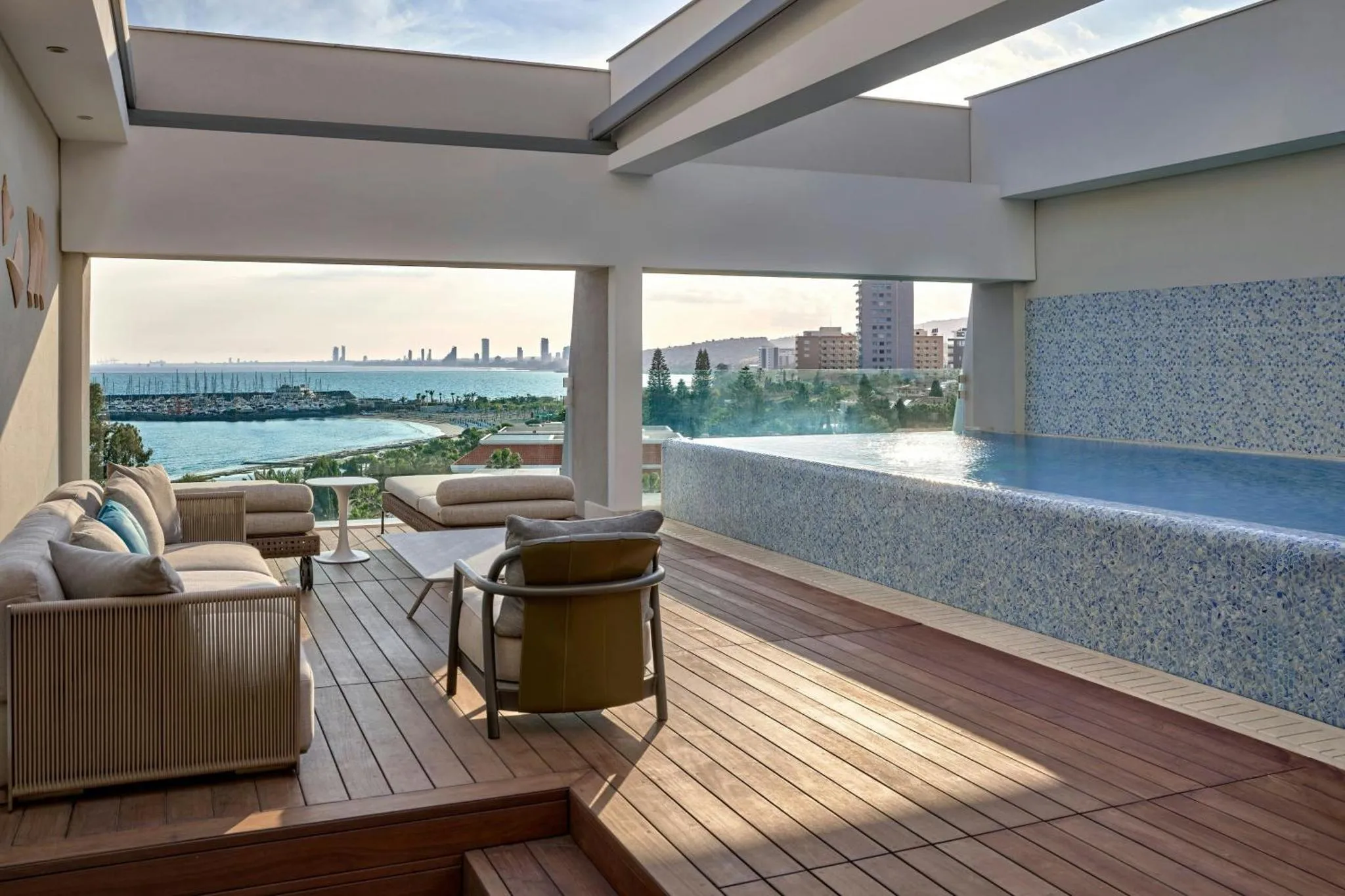 Espace de détente extérieur avec mobilier et piscine à débordement offrant une vue sur la mer.