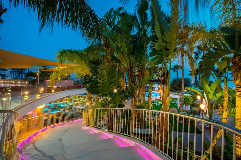Terrasse illuminée avec végétation tropicale et vue sur une piscine.