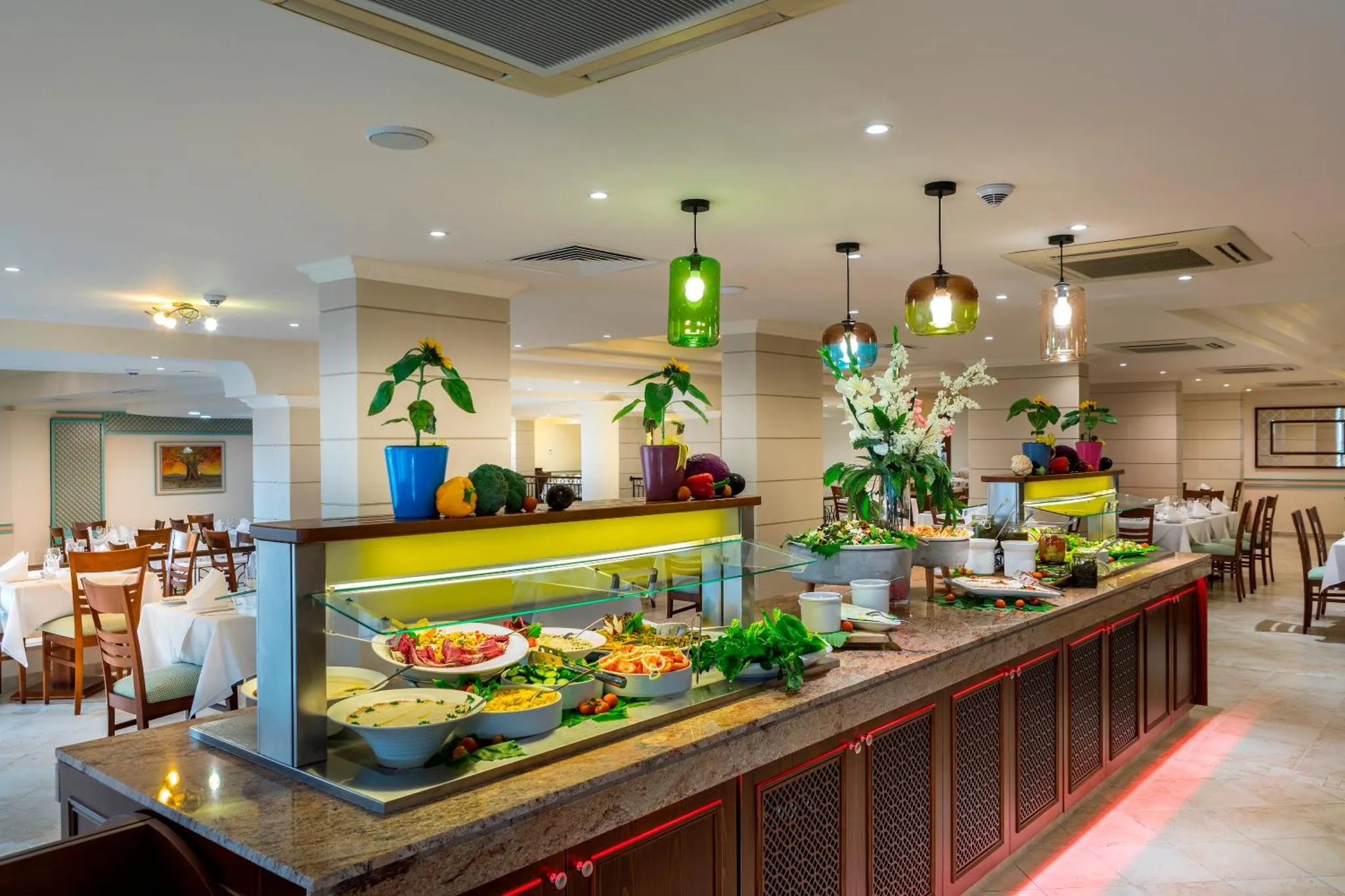 Un buffet de salades et de plats froids est présenté dans une salle lumineuse et décorée.