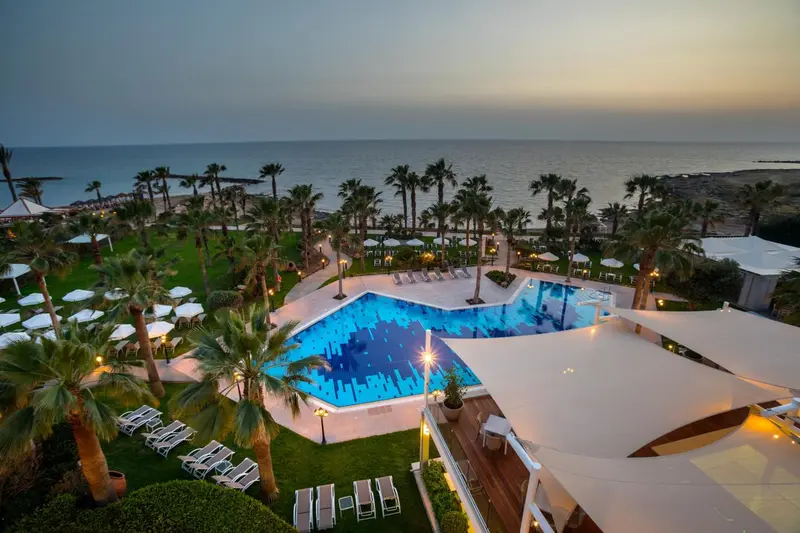Vue aérienne d'un complexe hôtelier avec piscine et végétation luxuriante face à la mer.