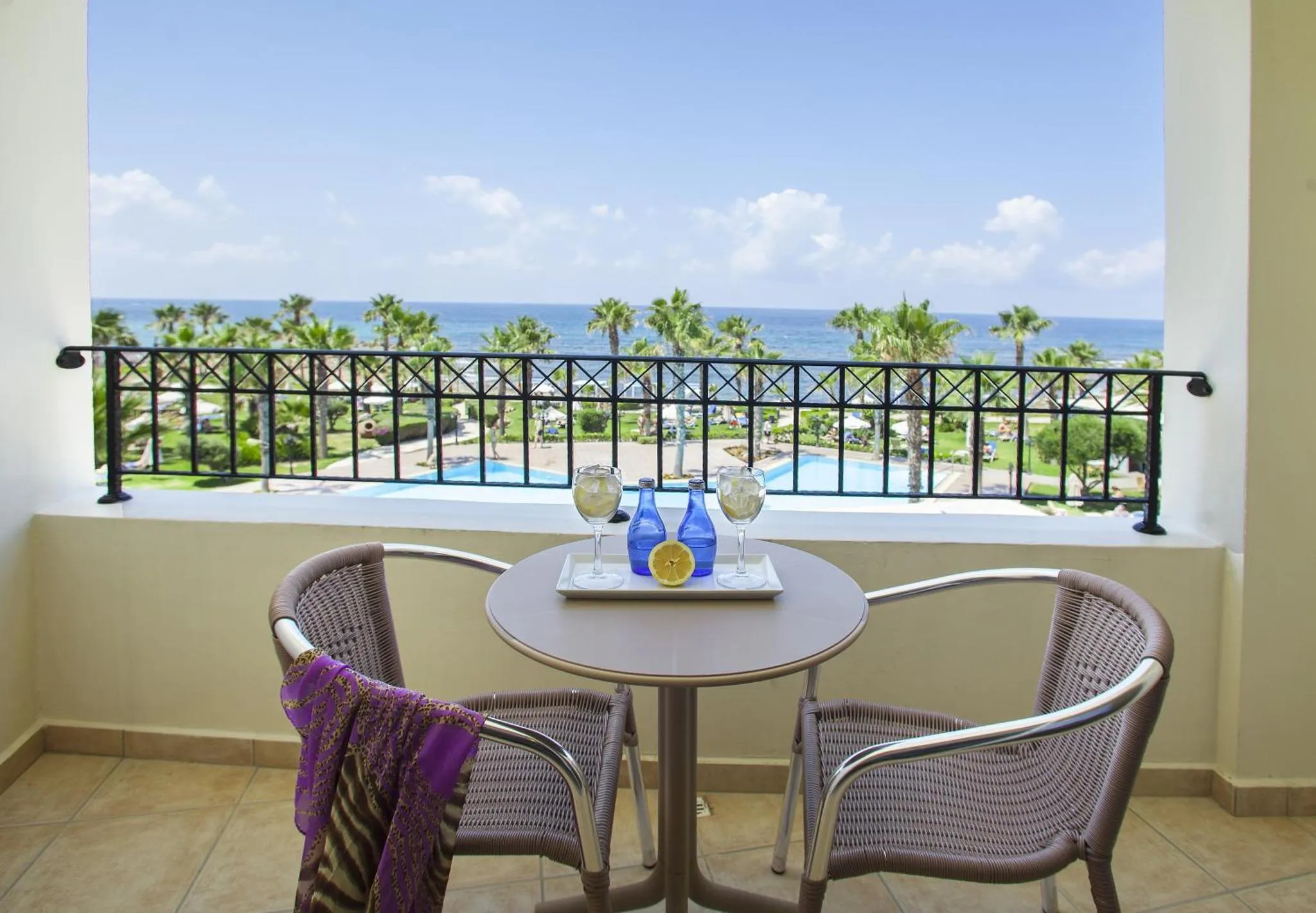 Une table ronde avec deux verres et des citrons sur une terrasse ensoleillée avec vue sur la mer.