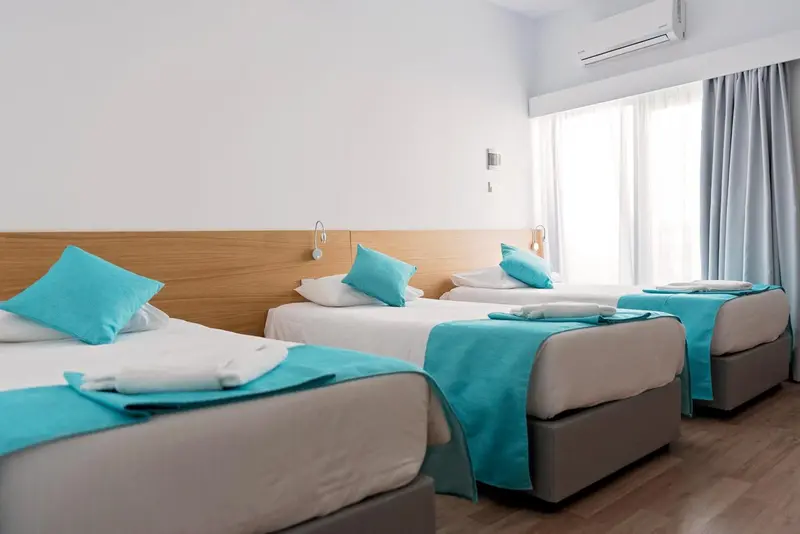 Chambre lumineuse avec deux lits simples turquoise et un rideau bleu.