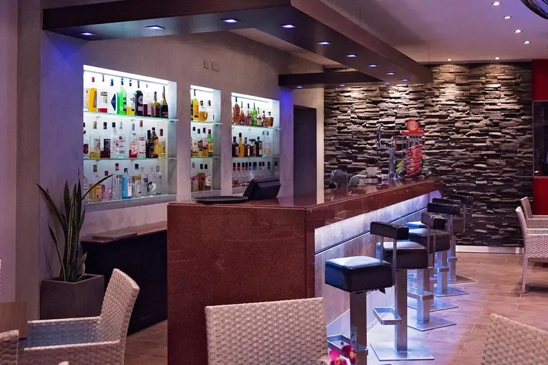 Un comptoir de bar moderne avec des bouteilles illuminées et des tabourets.