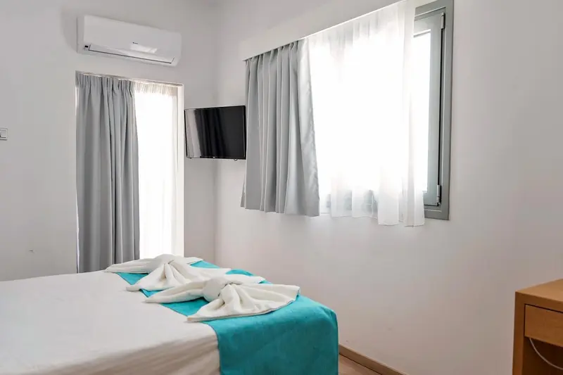 Une chambre lumineuse avec un lit fait et une télévision murale.