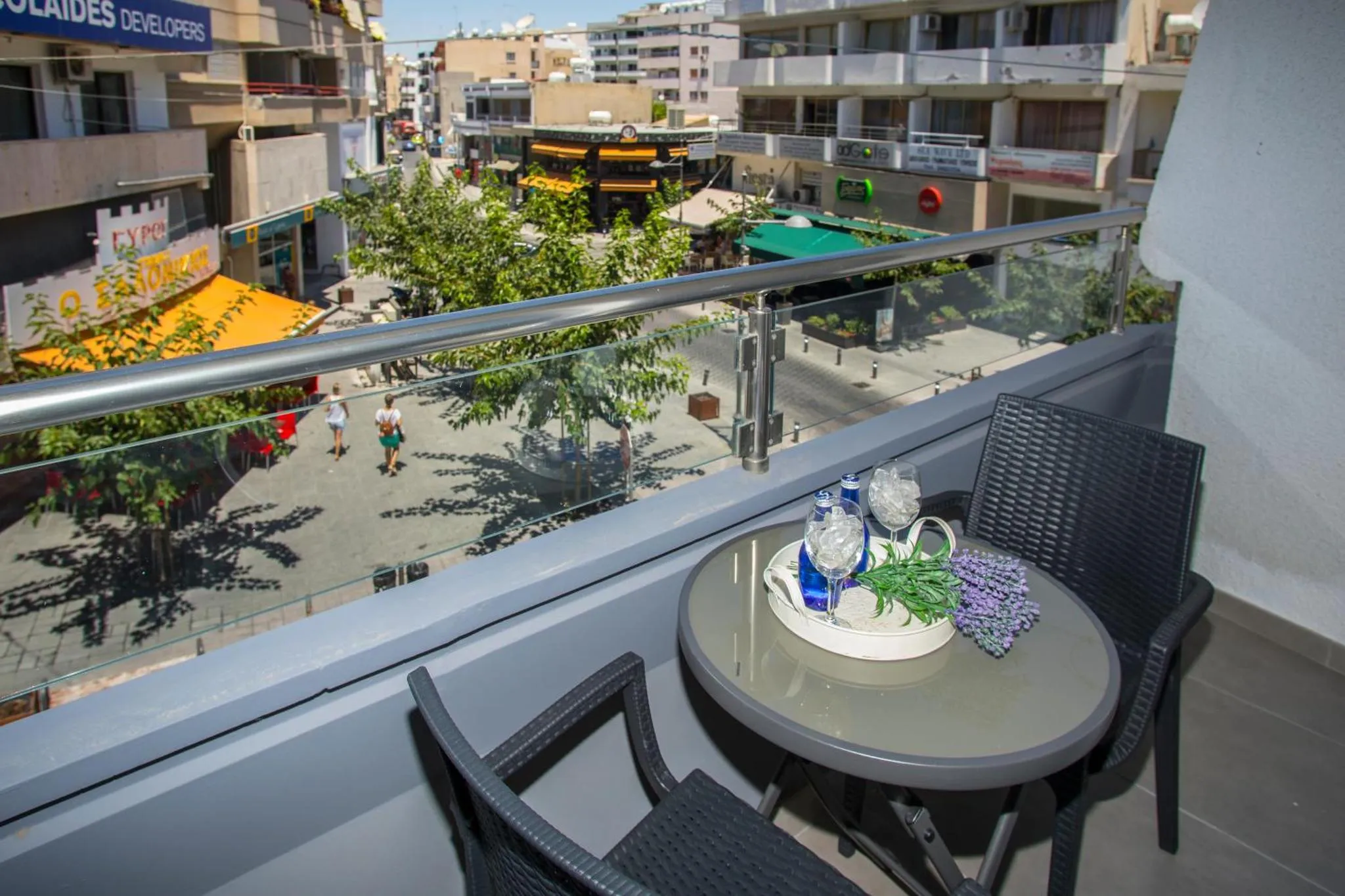 Une table ronde avec des boissons et des fleurs sur un balcon ensoleillé.