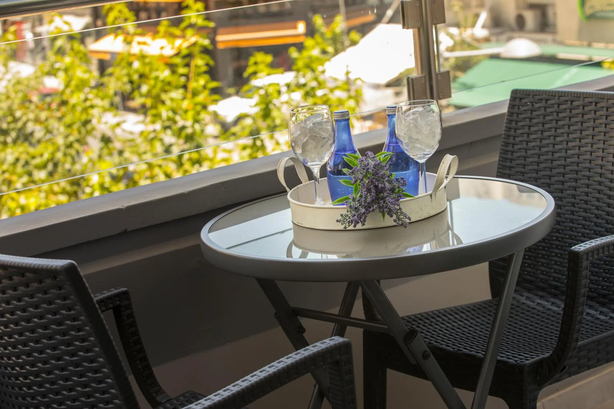 Une table ronde en verre avec des boissons et des fleurs sur une terrasse.