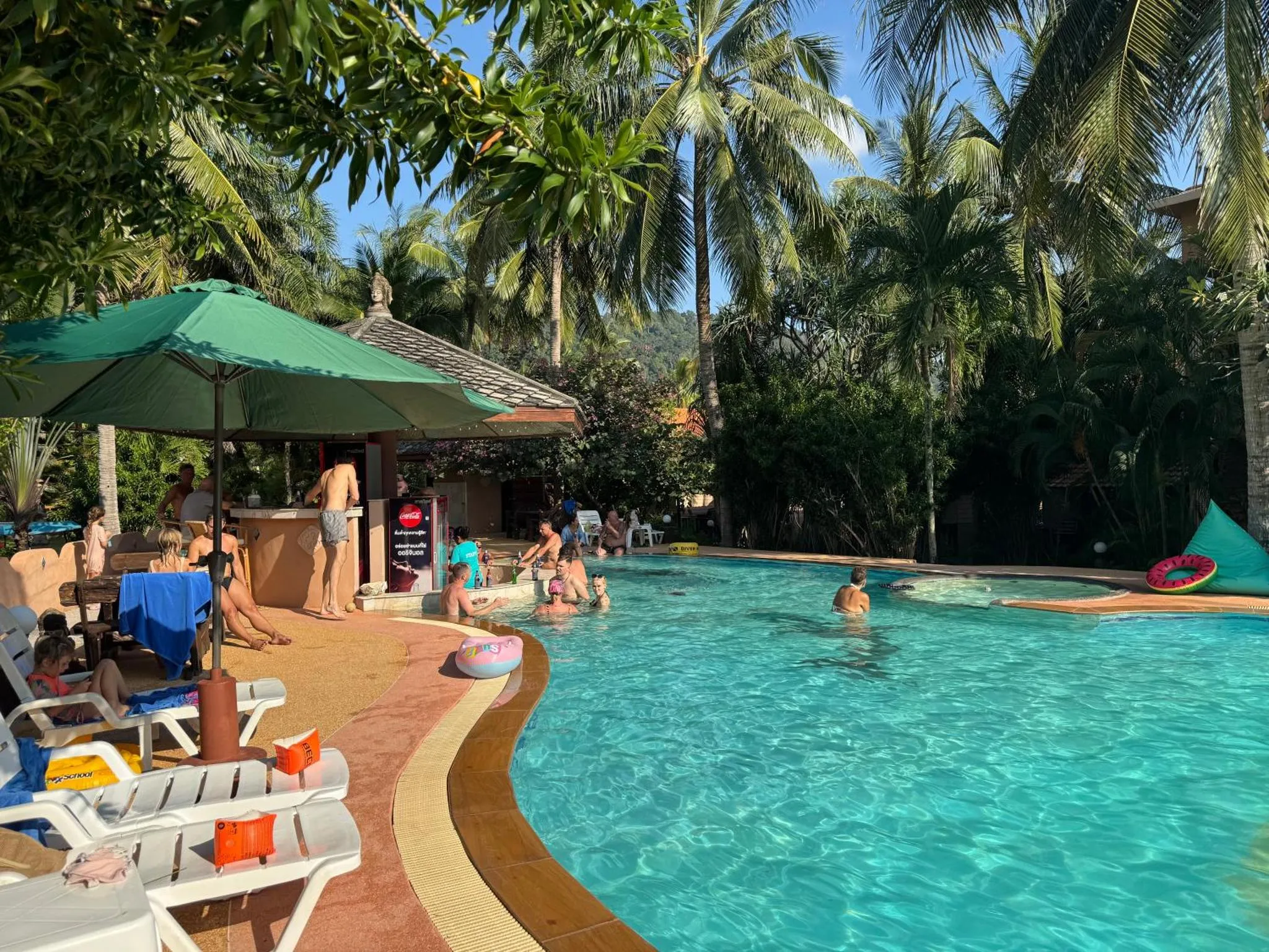 Une piscine bordée de transats et d'un bar ombragé.