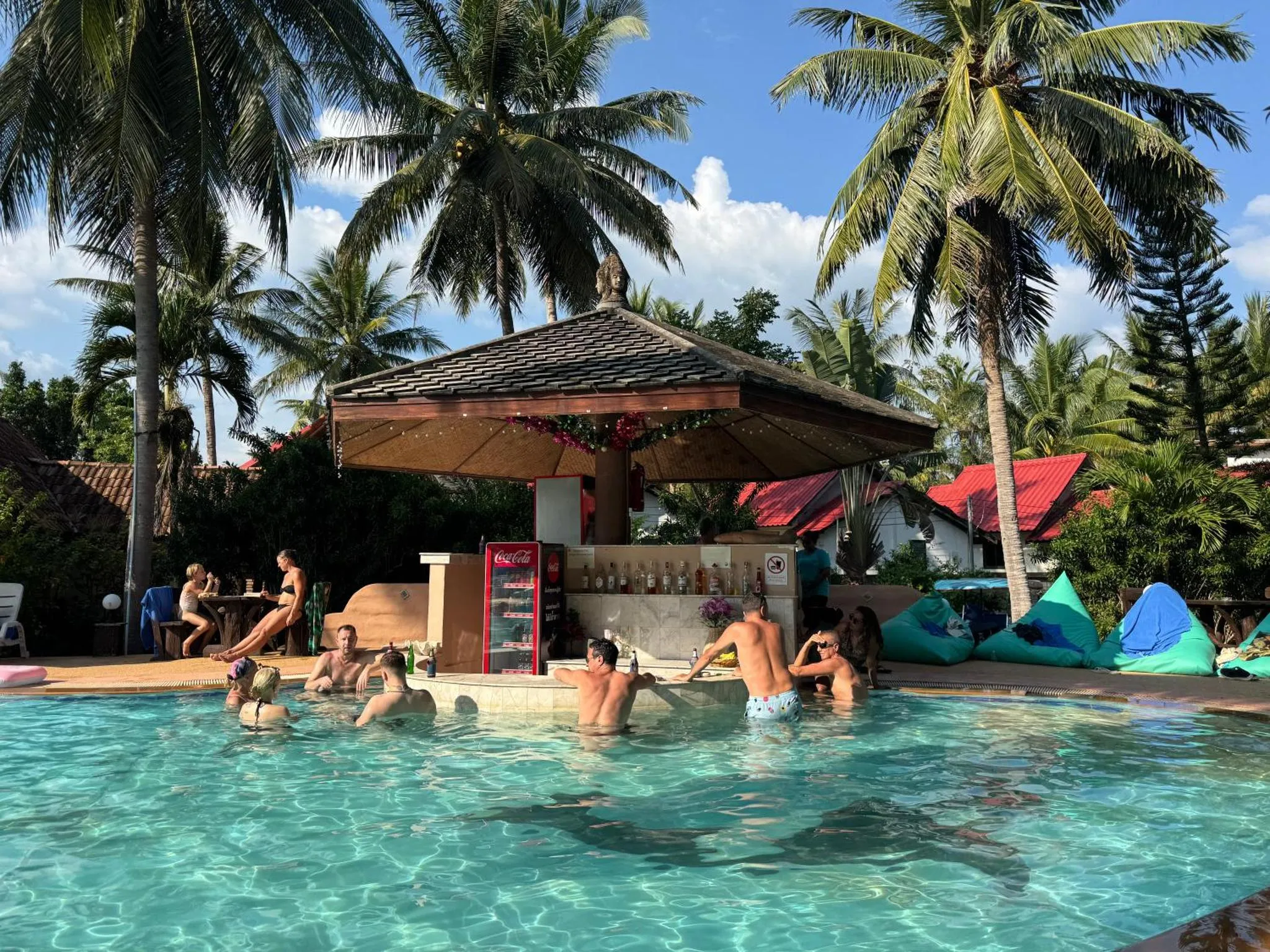 Des clients se rafraîchissent dans une piscine bordée de palmiers et d'un bar.