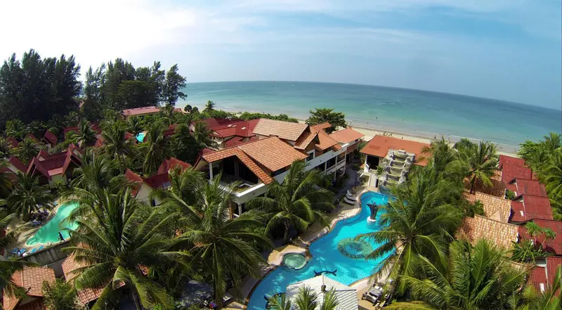 Vue aérienne d'un complexe hôtelier avec piscines et végétation tropicale face à une plage.