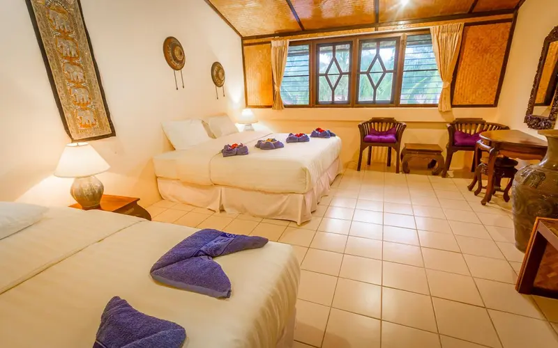 Une chambre lumineuse avec deux lits et un coin repas près d'une fenêtre.