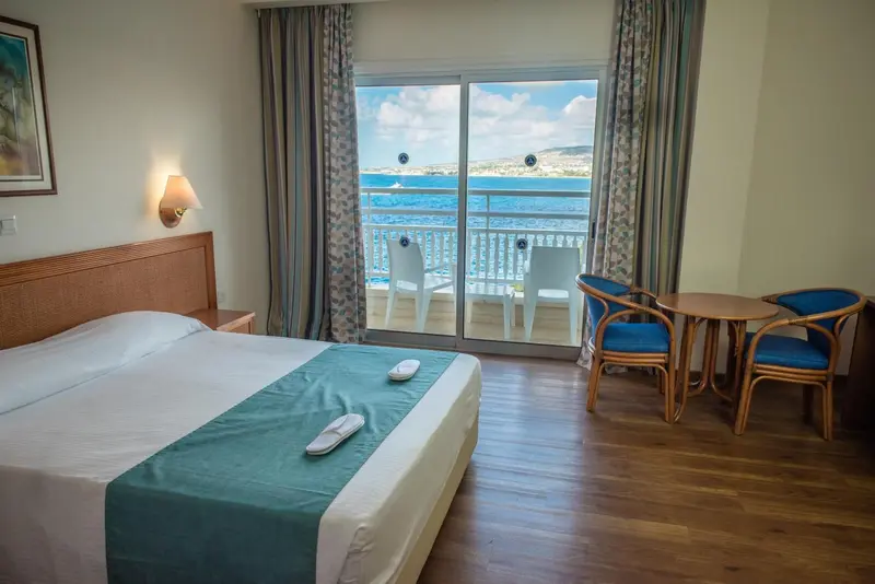 Chambre lumineuse avec un grand lit et une vue sur la mer depuis une terrasse.