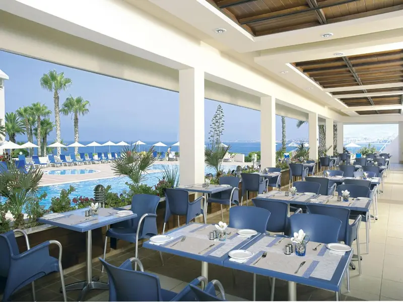 Une salle à manger lumineuse avec vue sur une piscine et la mer.