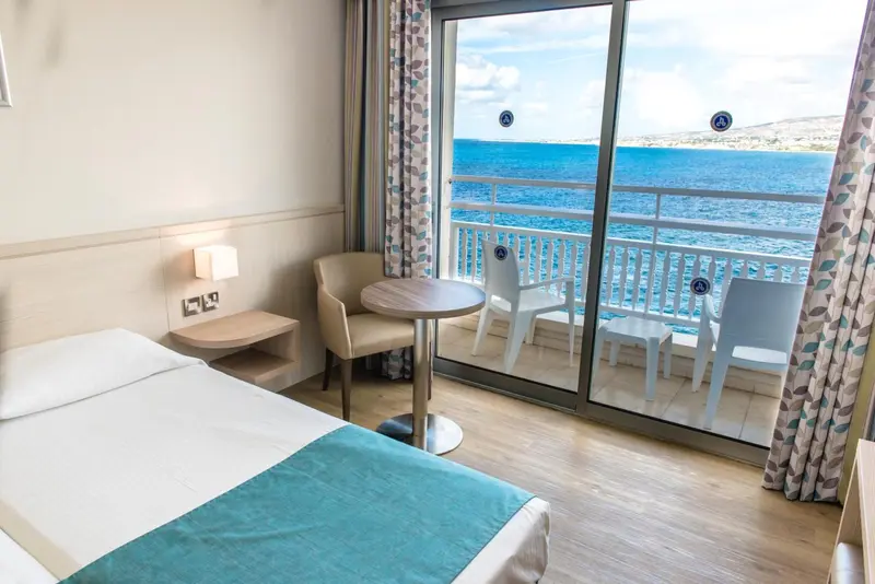 Chambre lumineuse avec vue sur la mer depuis un balcon.