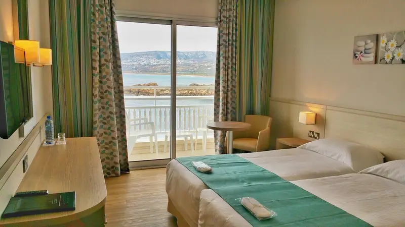 Une chambre lumineuse avec un lit et une vue sur la mer depuis un balcon.