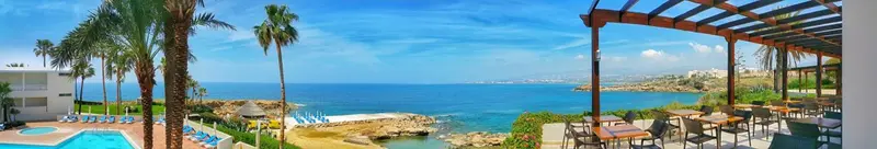 Vue sur la mer depuis une terrasse ombragée avec des tables et des chaises.