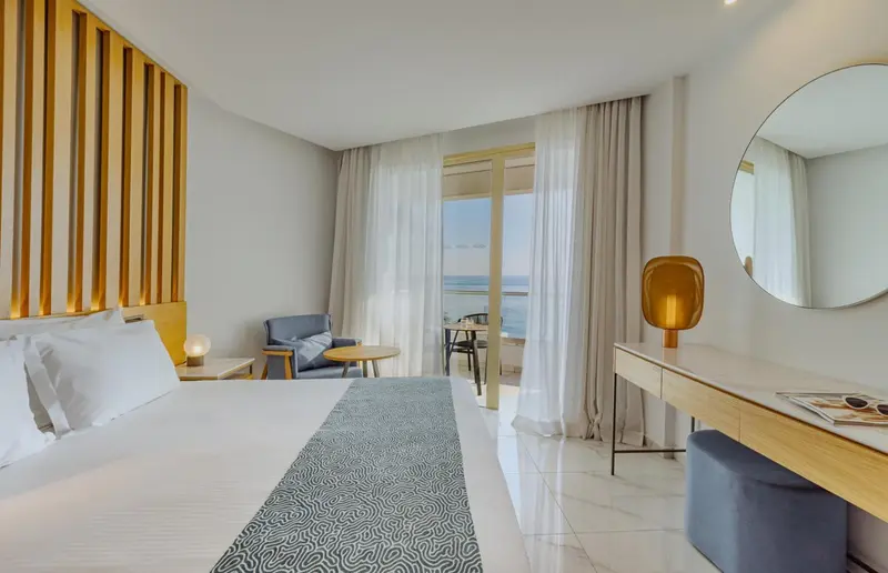Chambre lumineuse avec un lit fait et une vue sur la mer.