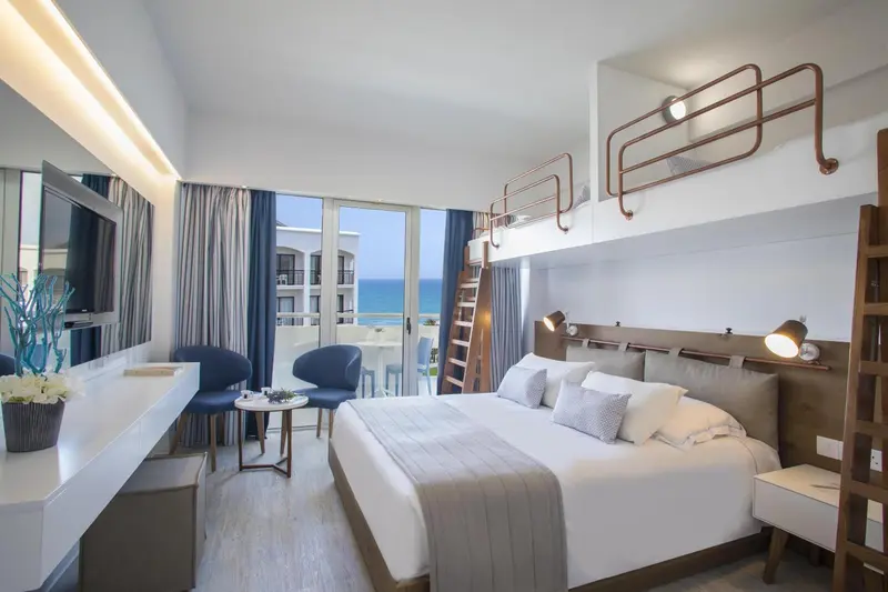 Chambre lumineuse avec un lit double et un lit superposé, donnant sur la mer.