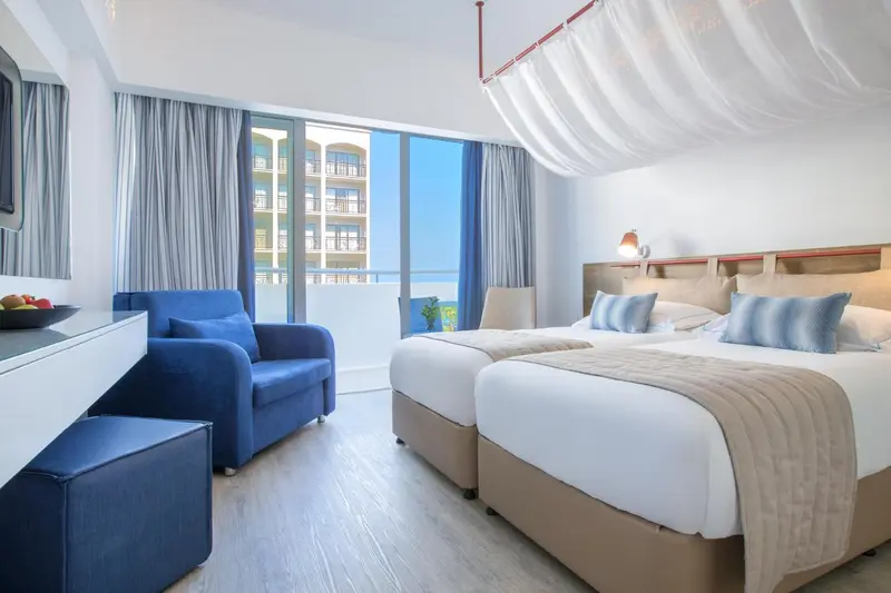 Chambre lumineuse avec deux lits simples et un coin salon.