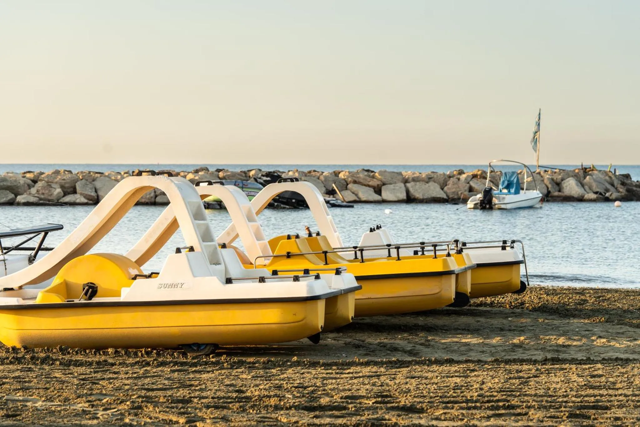 Plusieurs pédalos jaunes reposent sur une plage de sable fin face à la mer.