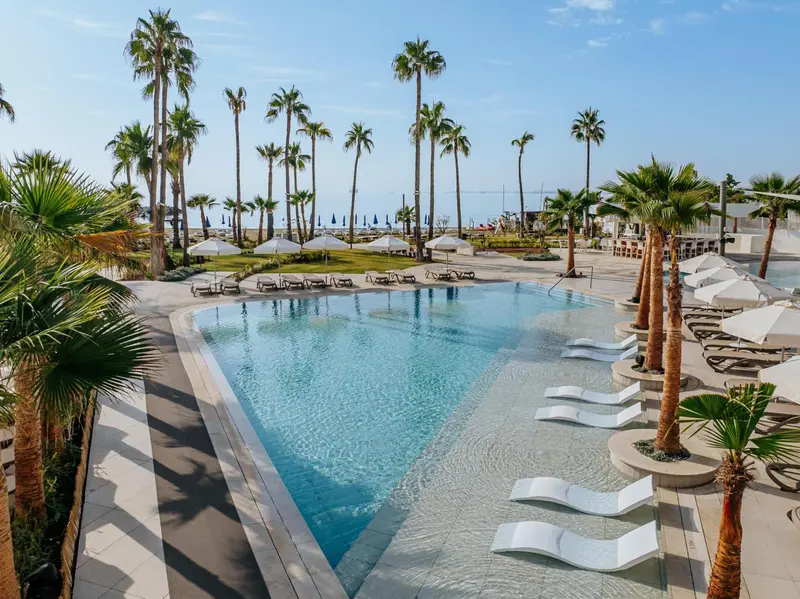 Une piscine rectangulaire bordée de transats blancs, avec des palmiers en arrière-plan.