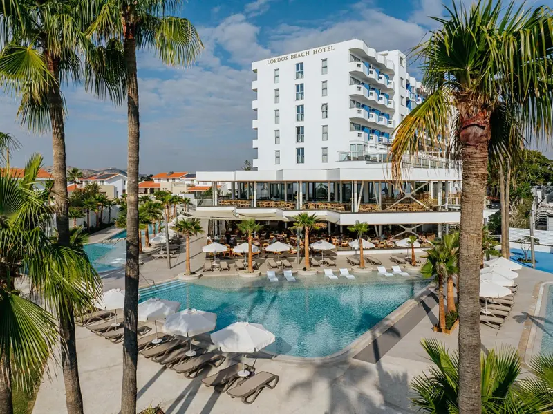 Vue d'un hôtel blanc avec piscine et palmiers.