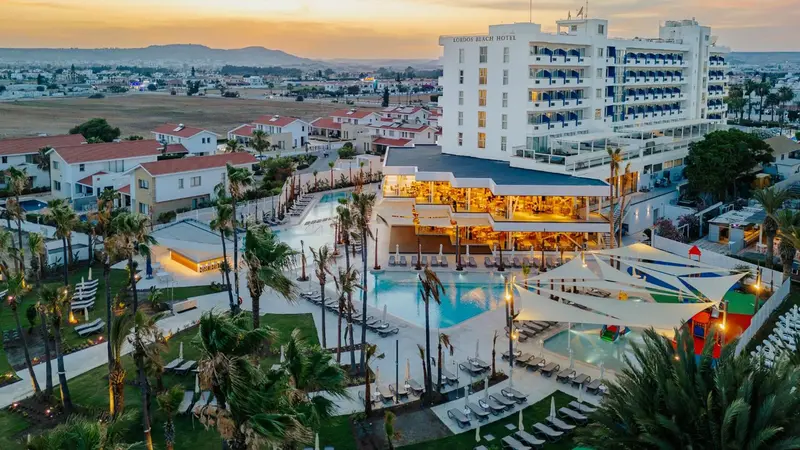 Vue aérienne d'un complexe hôtelier avec piscine et palmiers au coucher du soleil.