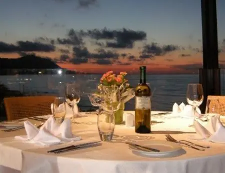 Table dressée avec une bouteille de vin et des verres face à la mer au coucher du soleil.