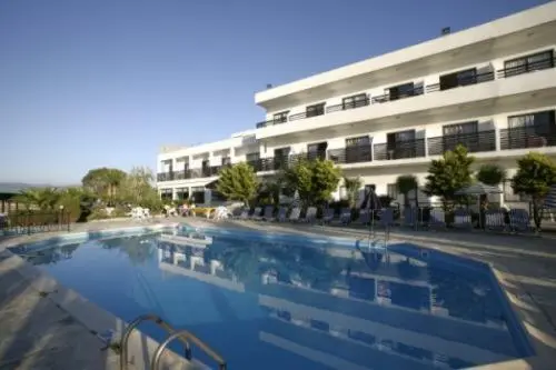 Piscine rectangulaire devant un bâtiment blanc à balcons.
