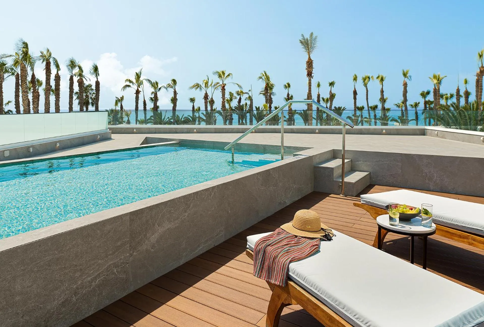 Terrasse avec piscine et transats, vue sur la mer et la végétation.