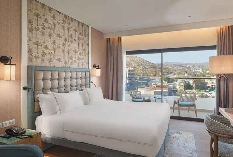 Chambre lumineuse avec un grand lit et vue sur un paysage montagneux.