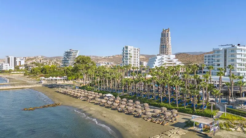 Vue aérienne d'une plage avec des transats et des parasols devant des bâtiments blancs.